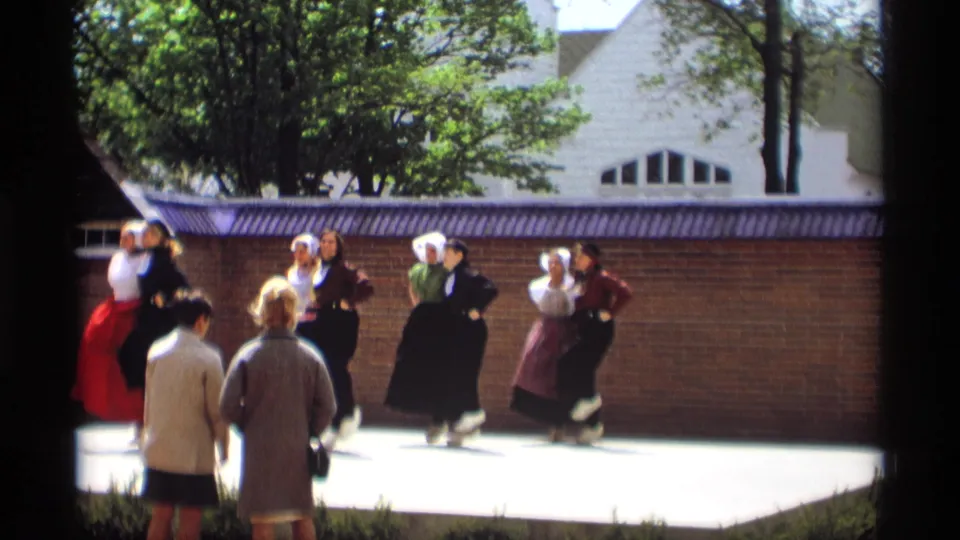 Women in Dutch-style folk costumes continue a synchronized outdoor dance in Holland, Michigan, with onlookers close to the performance area.