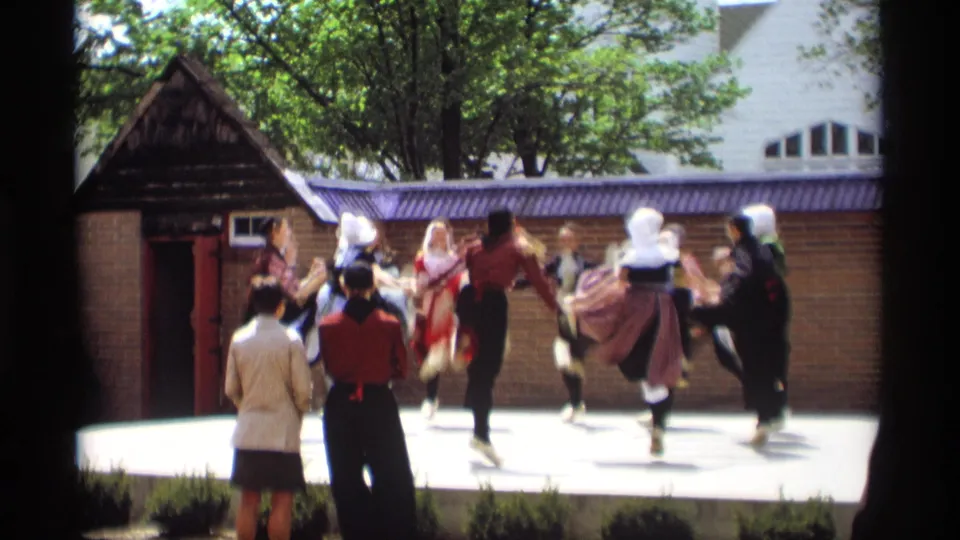 Costumed dancers in Holland, Michigan move energetically in a circle during a 1969 outdoor folk performance watched by nearby spectators.