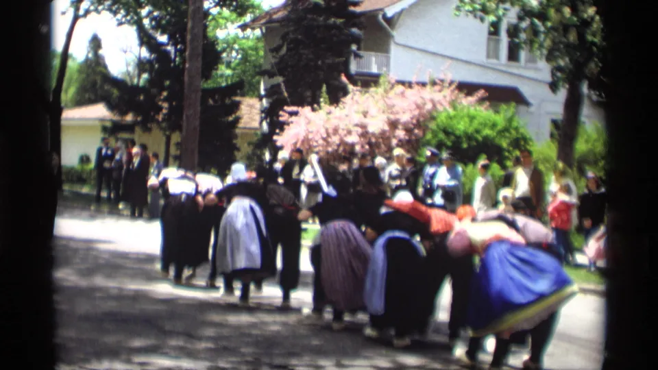 A group of women in traditional-style dress bends together during a 1969 Holland, Michigan street dance, with onlookers in the background.