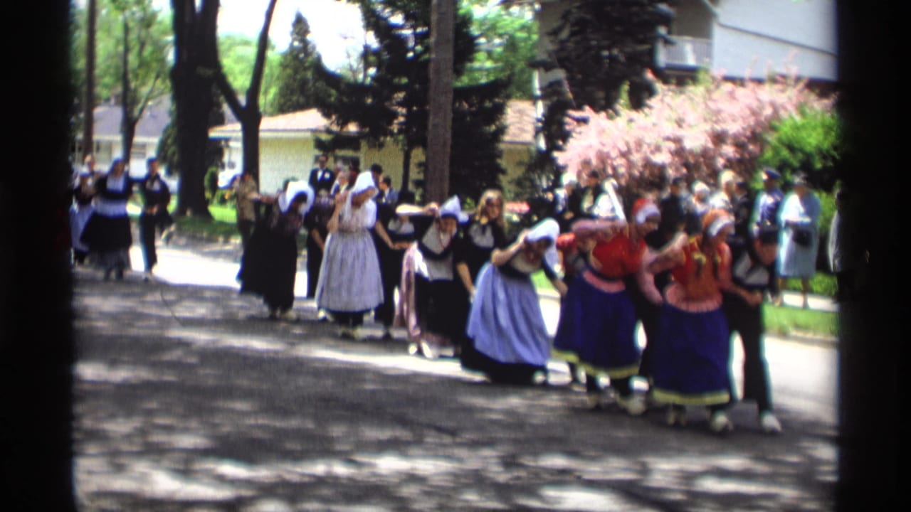 Women in traditional Dutch-style costumes march along a shaded street during a parade.