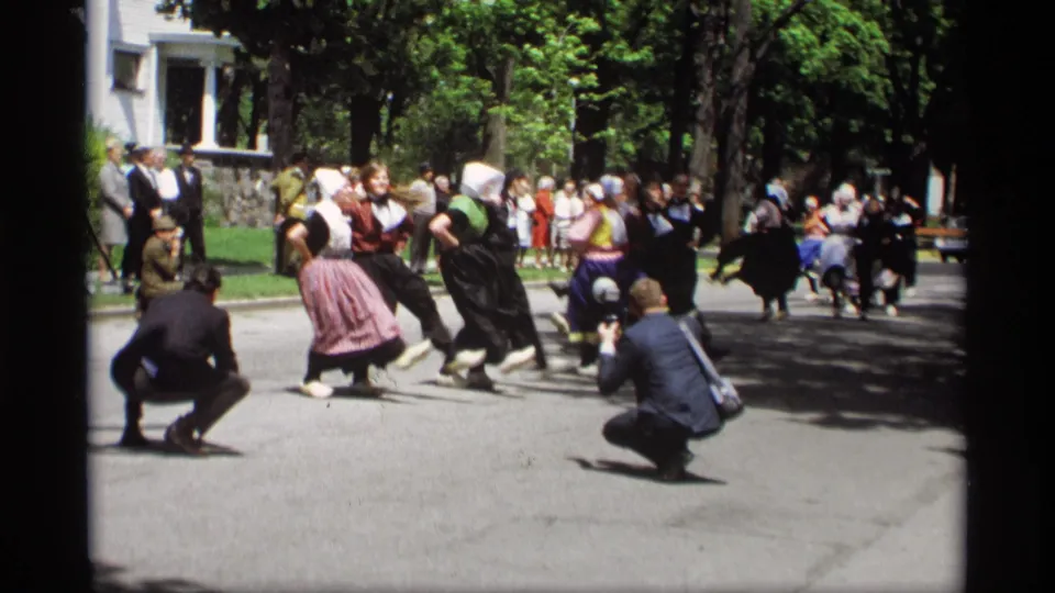 Dutch folk dancers in Holland, Michigan continue their 1969 street performance, with photographers and spectators visible around them.