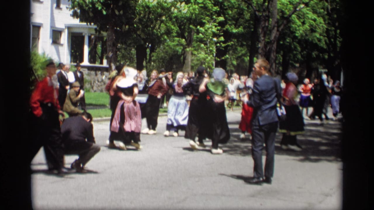 Dancers in traditional clothing move across the street before spectators.