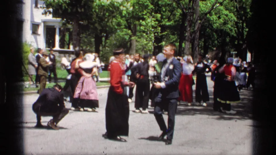 Street-level 8mm view of Dutch-style folk dancers in Holland, Michigan, with photographers crouching and standing nearby.