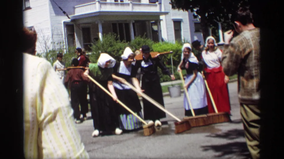 Holland, Michigan footage from 1969 shows women in traditional-style dress sweeping a street, with spectators and a white house behind them.