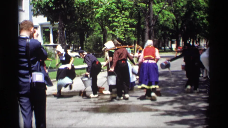 The final frame shows the Holland, Michigan street activity from farther back, with costumed participants, buckets, trees, and spectators filming.