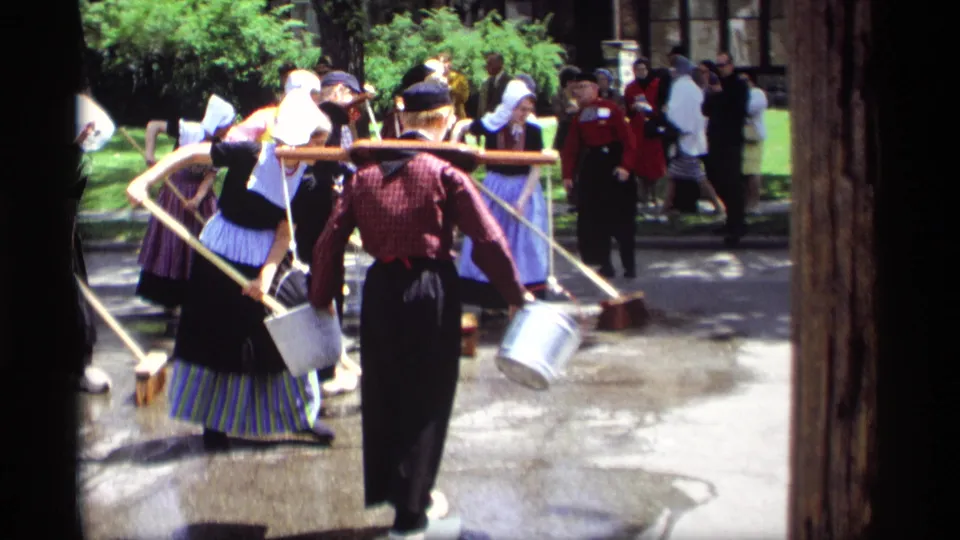 1969 Holland, Michigan frame showing Dutch-style costumed participants with buckets and brooms during a street-cleaning demonstration.
