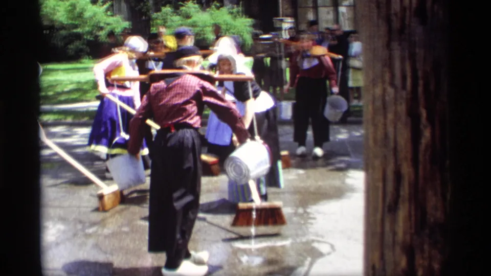 Traditional Dutch-style street-cleaning activity continues in Holland, Michigan, with brooms, buckets, wet pavement, and spectators visible.