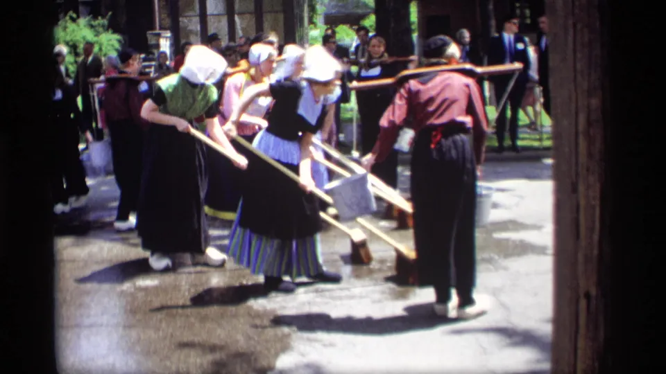 1969 street scene in Holland, Michigan showing women in Dutch-style dress sweeping near a man with a bucket and nearby spectators.