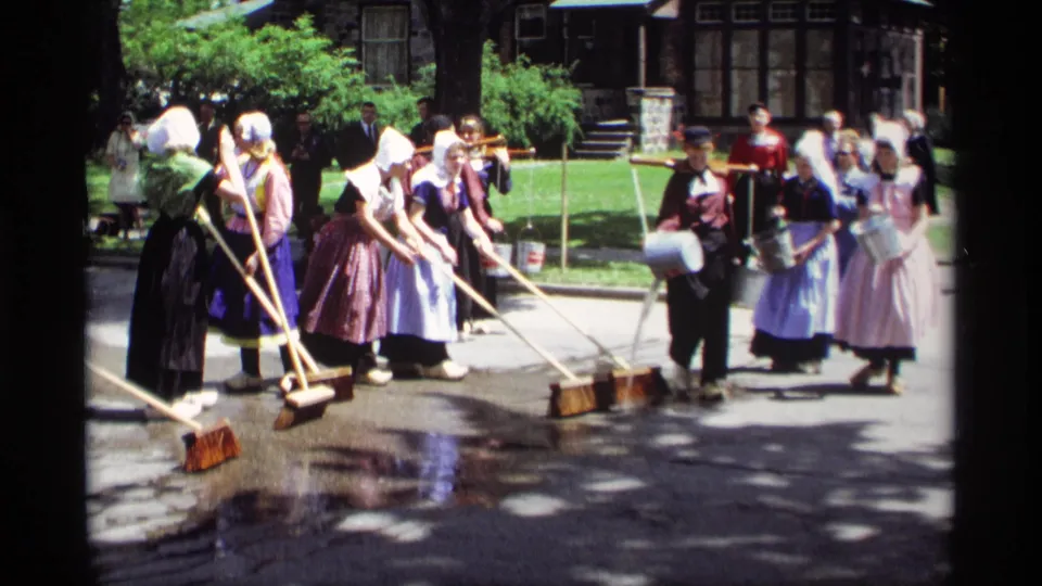 1969 Holland, Michigan frame showing costumed women with brooms and buckets during an outdoor Dutch heritage street-washing demonstration.