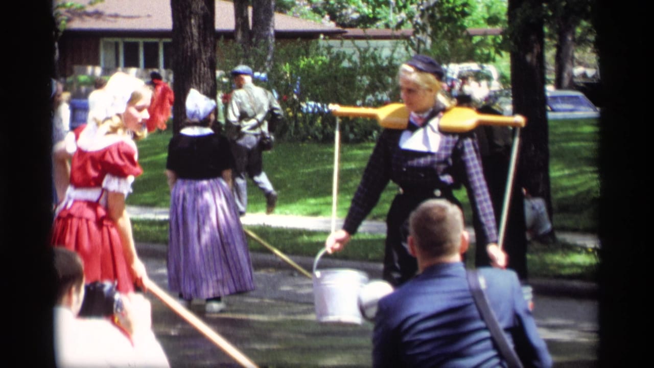 In Holland, Michigan in 1969, women in Dutch-style costumes move past spectators with a wooden yoke, metal buckets, and long poles.