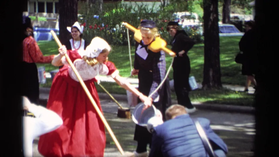 During the 1969 Holland, Michigan festival, a costumed woman bends forward with a long pole while another stands nearby with a yoke and bucket.