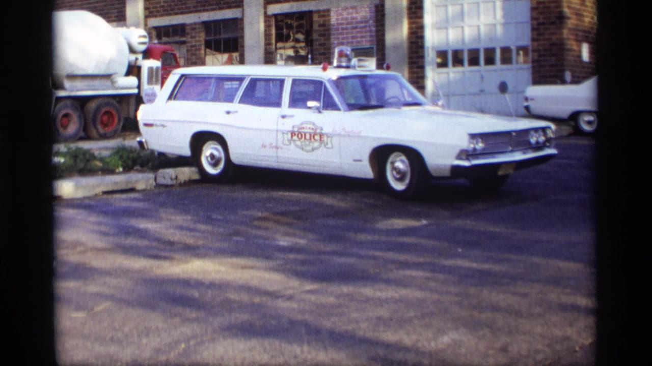 White police station wagon parked in front of a brick building with a cement mixer nearby.