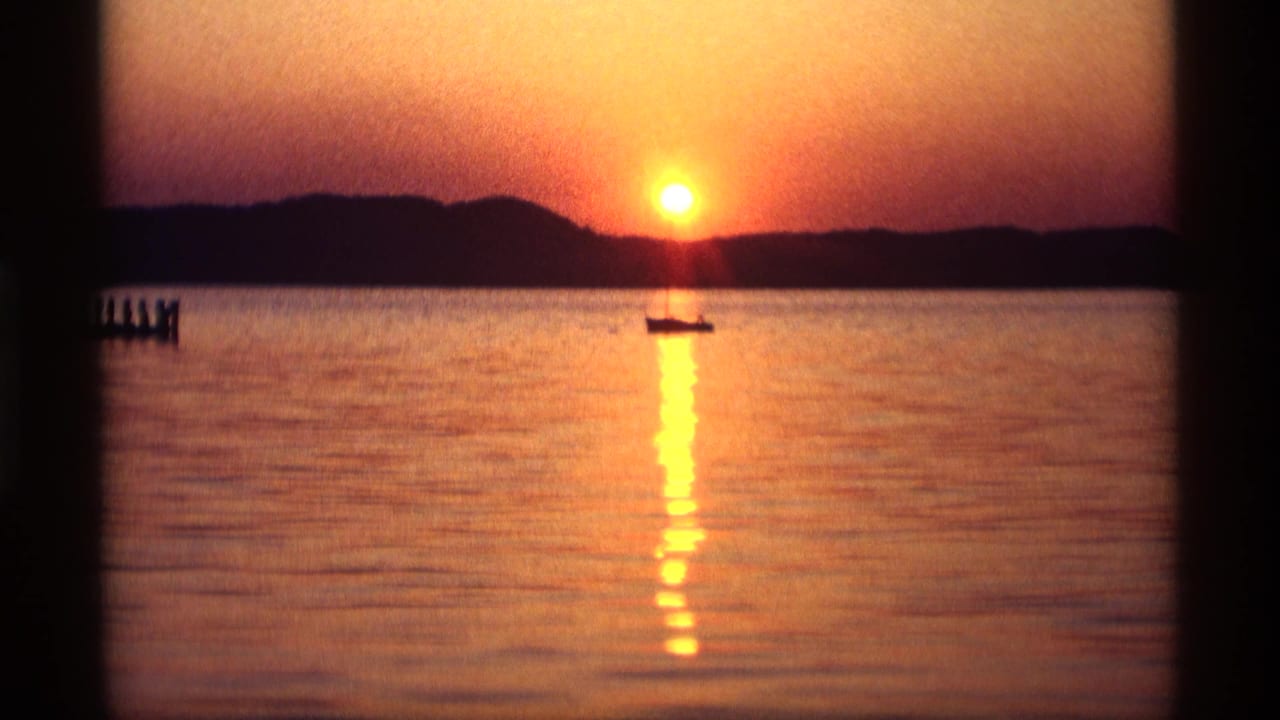 Orange sunset over calm water with a small boat silhouette and pier at left.
