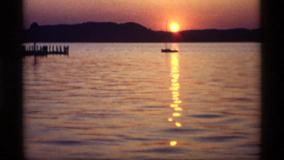 1969 Holland, Michigan 8mm frame with the sun near the horizon, a sailboat on the water, and a pier extending from the left.