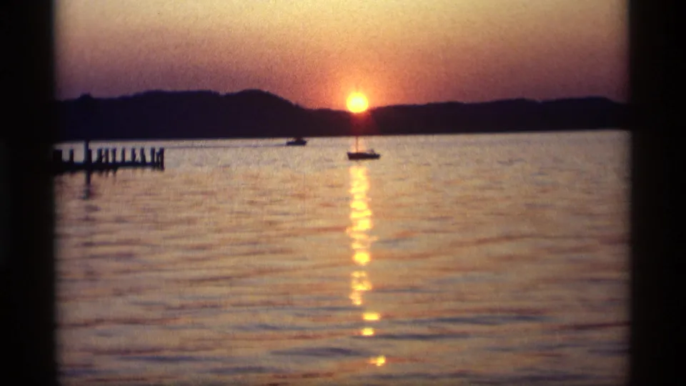 1969 Holland, Michigan 8mm frame with a glowing sunset, long water reflection, small sailboat, and pier silhouetted at left.