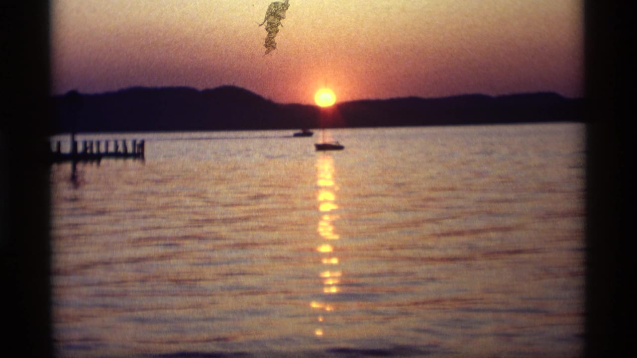 Sunset over calm lake water with small boats and a pier at left.