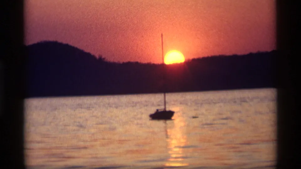 The sunset view continues with a small sailboat and mast silhouetted against orange light over the lake in 1969 home-movie footage.