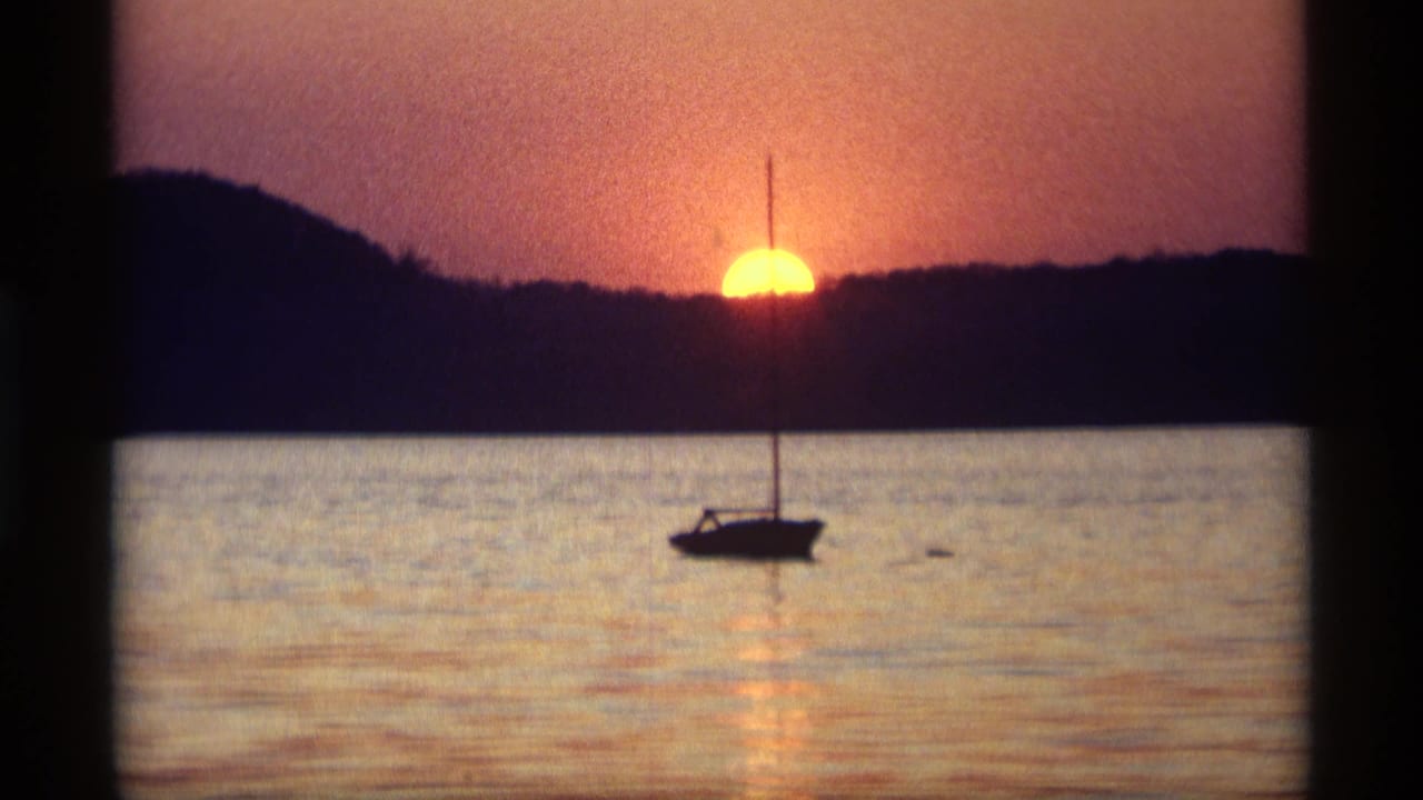 1969 Holland, Michigan 8mm frame showing a small sailboat in silhouette on calm water as the sun drops behind a dark shoreline.