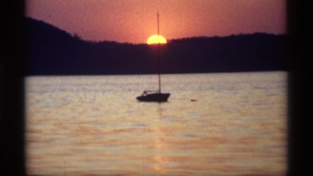 Sailboat silhouette on rippled water with the setting sun behind the shore.