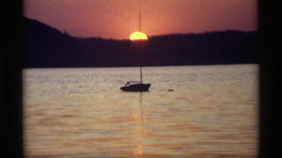 1969 Holland, Michigan 8mm frame of a small sailboat silhouetted against calm water and a low sunset behind the shoreline.