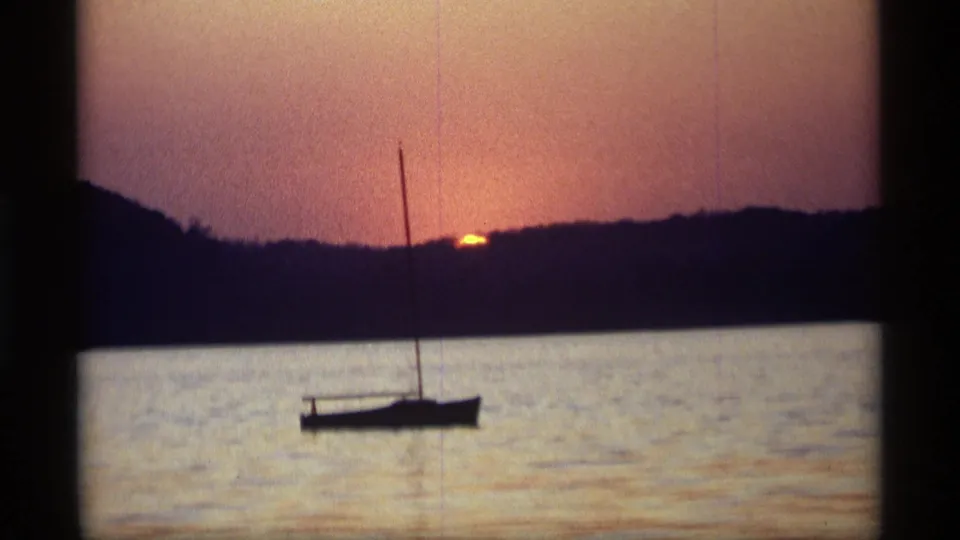 Vintage 8mm frame from Holland, Michigan in 1969 showing a quiet sailboat silhouette below a warm sunset sky.