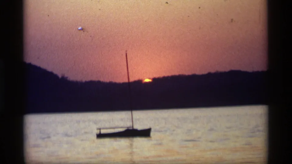 1969 Holland, Michigan 8mm still showing a silhouetted sailboat, calm water, and a nearly set sun beyond the tree-lined shore.