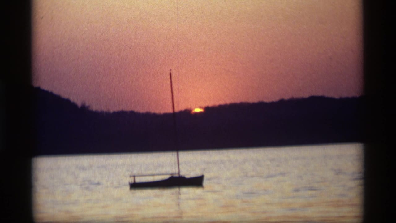 1969 Holland, Michigan 8mm frame showing a small sailboat in silhouette on calm water below an orange sunset sky.