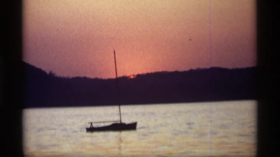 The final 1969 Holland, Michigan frame shows the sailboat in silhouette below a warm sunset and dark wooded horizon.