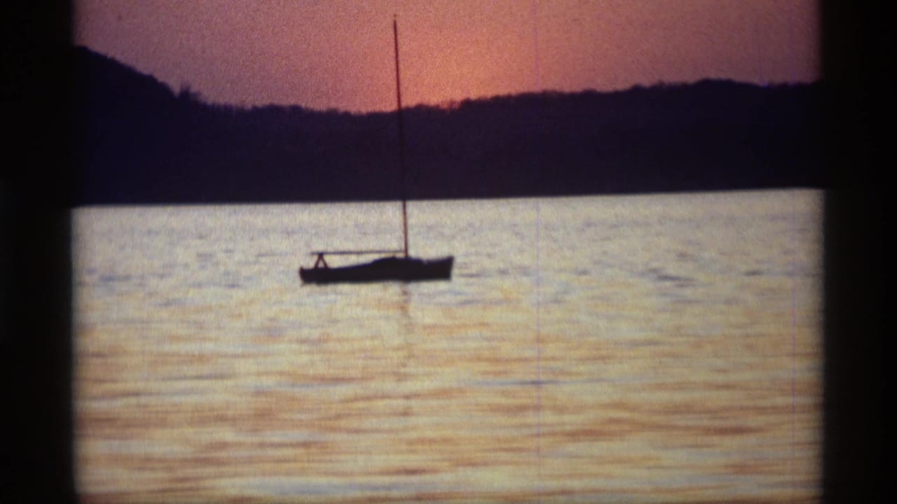 1969 Holland, Michigan 8mm frame showing a small sailboat silhouetted on a lake beneath orange-purple sunset light.