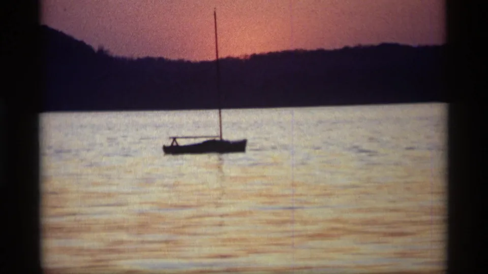 1969 Holland, Michigan 8mm frame showing a small sailboat silhouetted on a lake beneath orange-purple sunset light.