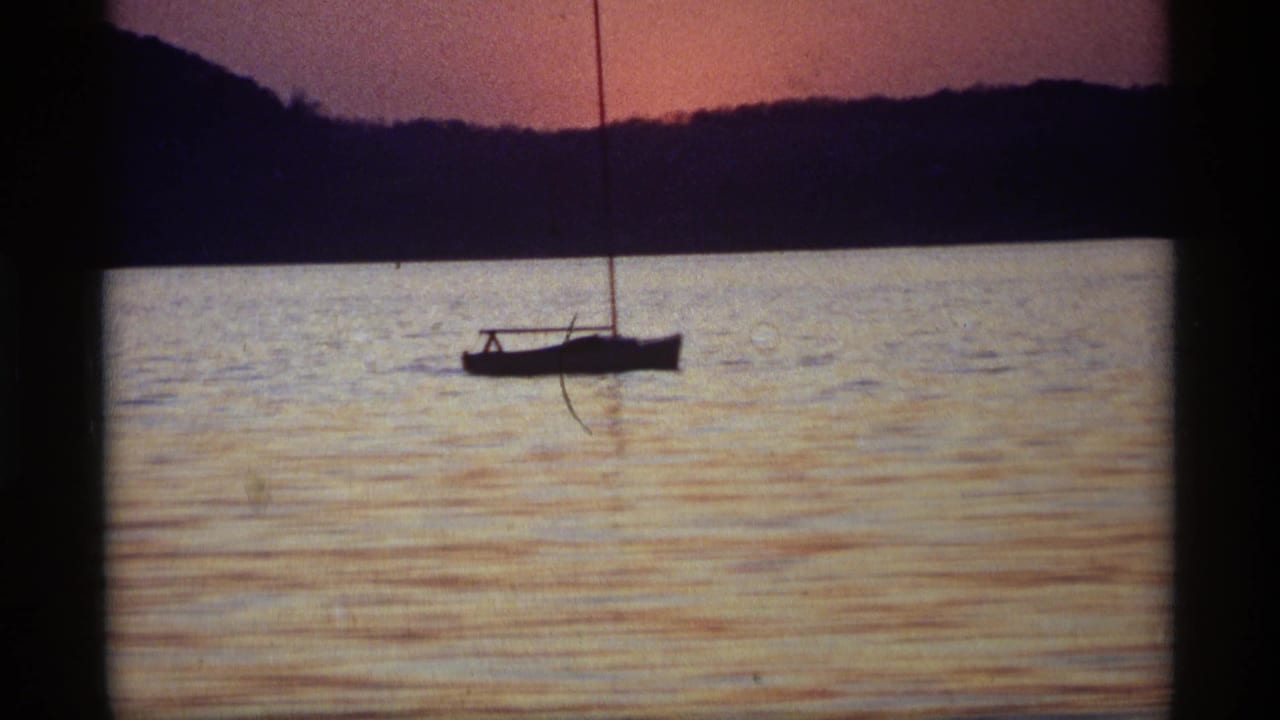 1969 Holland, Michigan frame with a sailboat near the horizon, reflective water, and dark shoreline under fading sunset color.