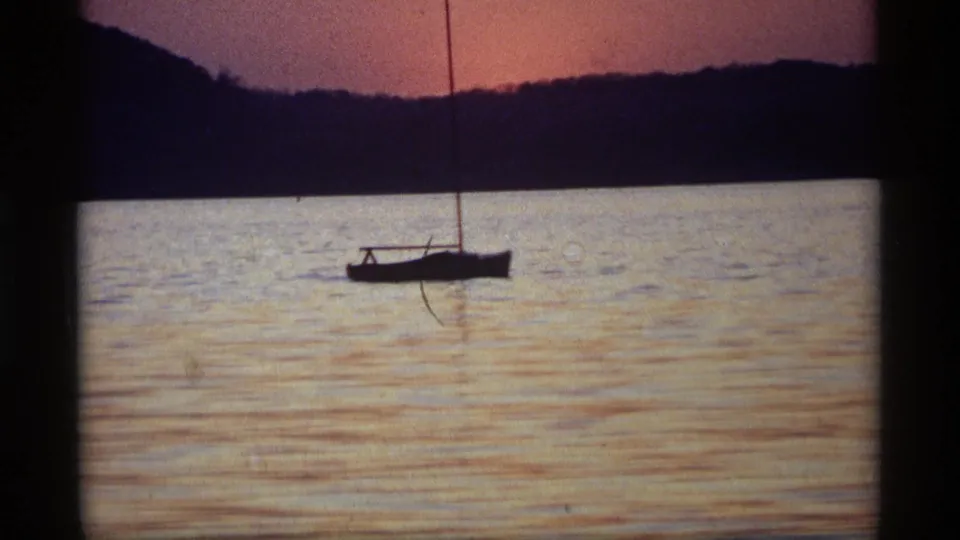 1969 Holland, Michigan frame with a sailboat near the horizon, reflective water, and dark shoreline under fading sunset color.