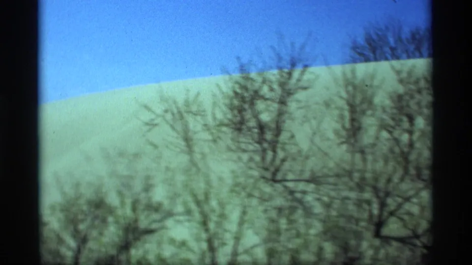 1969 Holland, Michigan 8mm frame showing a broad snow-covered hill, clear blue sky, and leafless trees in the foreground.