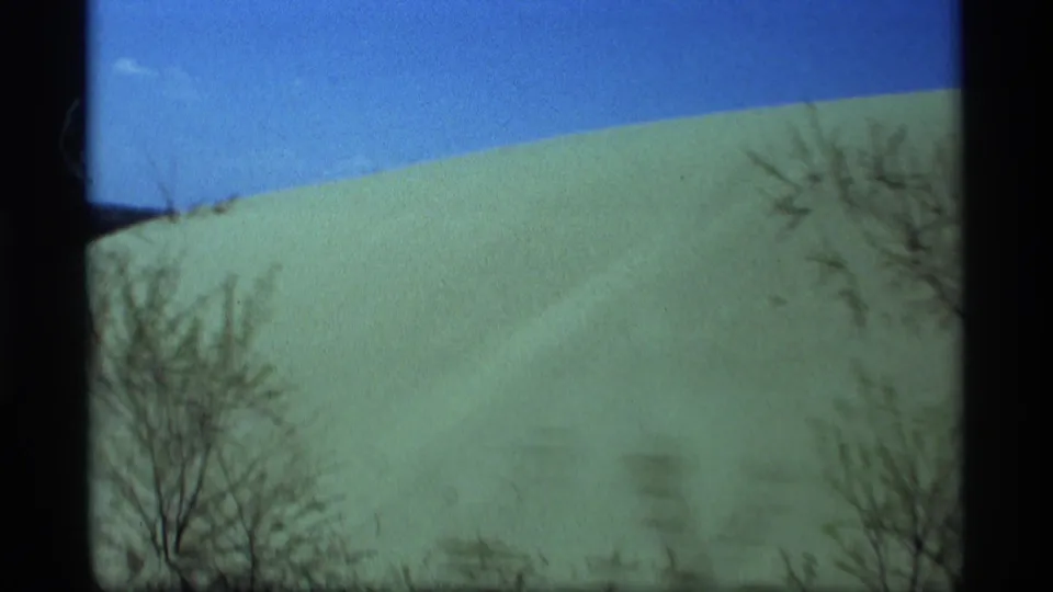 1969 Holland, Michigan frame showing a pale snow-covered slope, blue sky, and bare winter trees with visible 8mm frame edges.