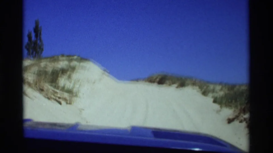 1969 Holland, Michigan home-movie view from a blue car approaching pale sand dunes beneath a clear sky.