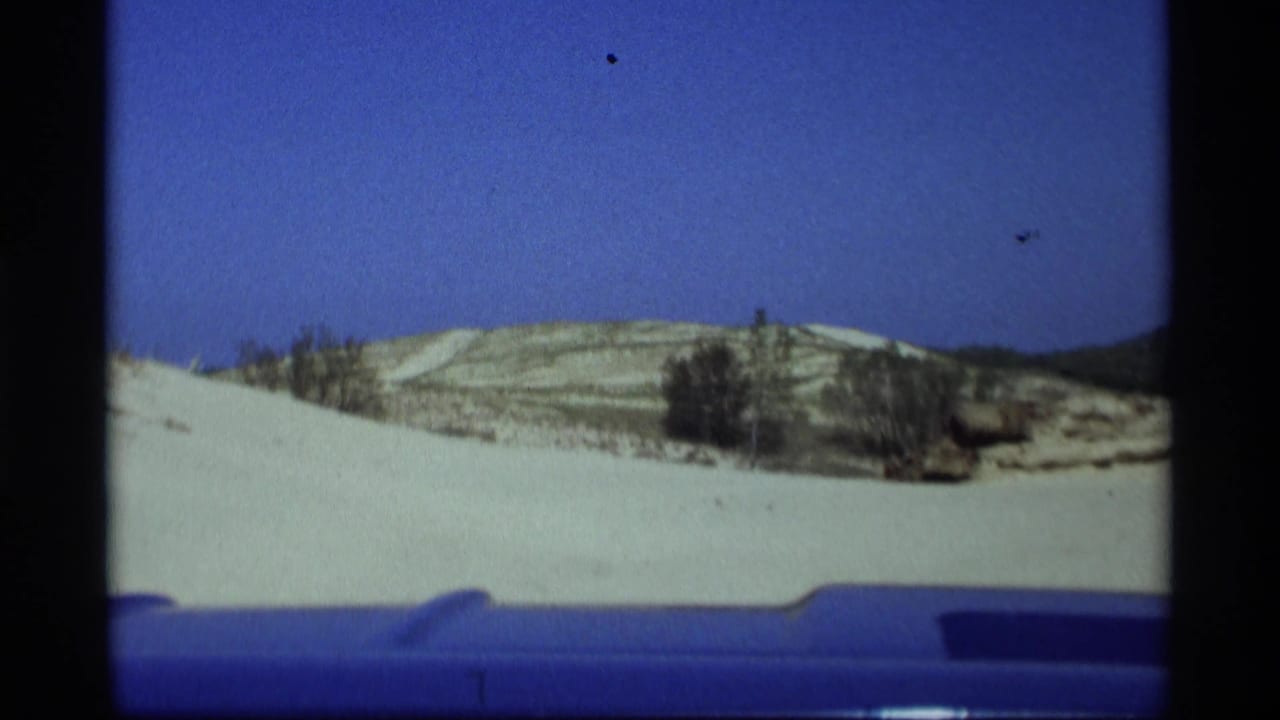 1969 Holland, Michigan home-movie frame showing sandy dunes and low hills from a vehicle-based viewpoint.