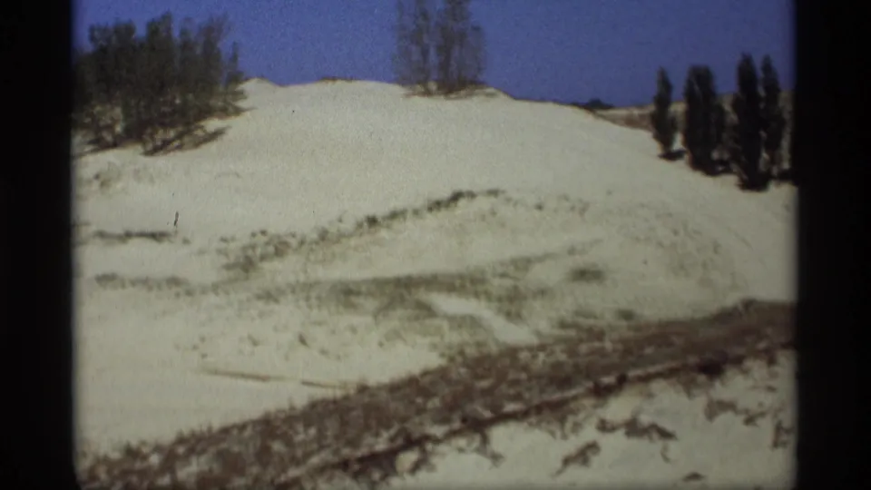 1969 Holland, Michigan 8mm frame showing a snow-covered rise with sparse trees and shrubs under a blue sky.