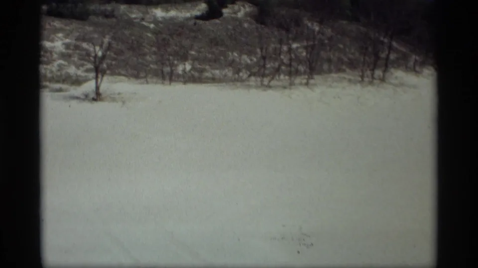 1969 home-movie view of an open snow field near Holland, Michigan, bordered by bare trees and darker low hills.