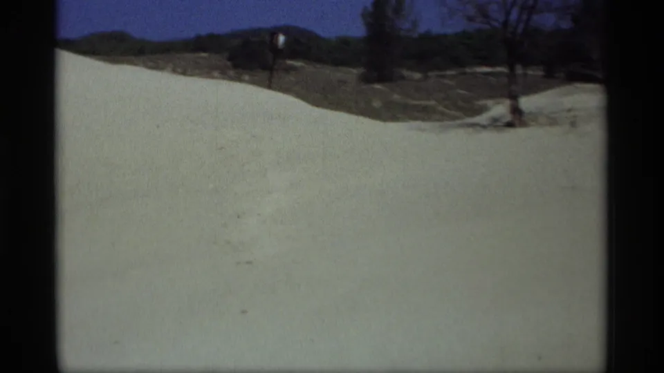 1969 8mm frame from Holland, Michigan showing a broad snowy area, road edge, bare trees, and distant low hills under blue sky.