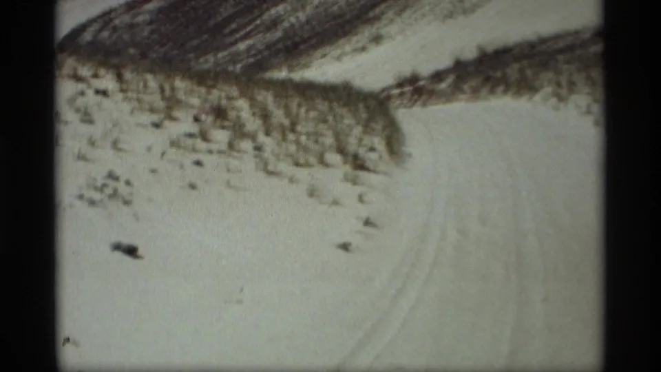1969 8mm frame from Holland, Michigan showing a snowy path and dune grass on rolling winter terrain.