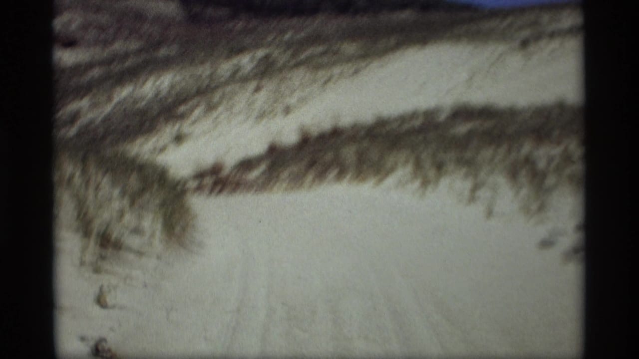 1969 8mm frame from Holland, Michigan showing a pale snow path winding through low wooded hills.