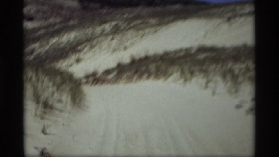 1969 8mm frame from Holland, Michigan showing a pale snow path winding through low wooded hills.