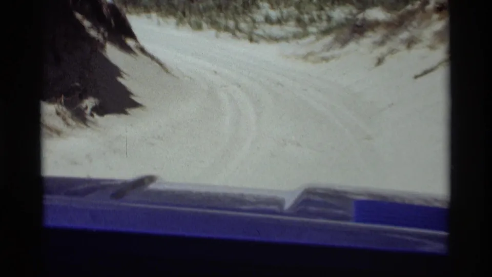 From a moving vehicle or passenger viewpoint, the 1969 8mm frame shows a snowy route through wooded hills near Holland, Michigan.