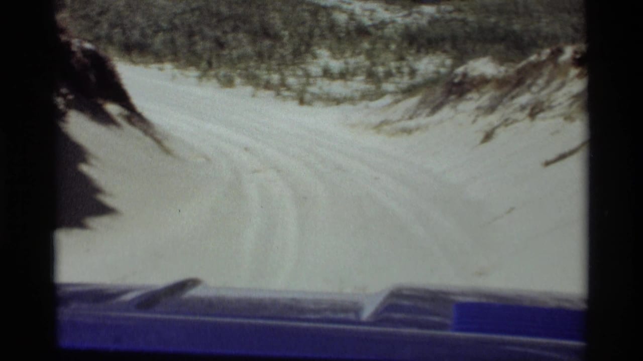 View over a blue vehicle dashboard toward a sandy road curving through dune grass.