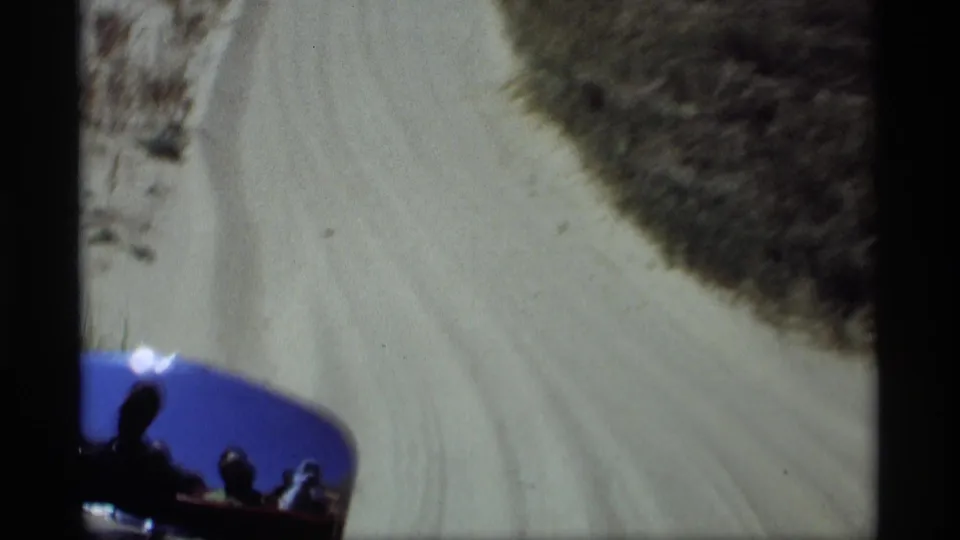 Passenger-perspective 1969 Holland, Michigan dune drive with sandy tracks ahead and small silhouetted people visible in the vehicle.