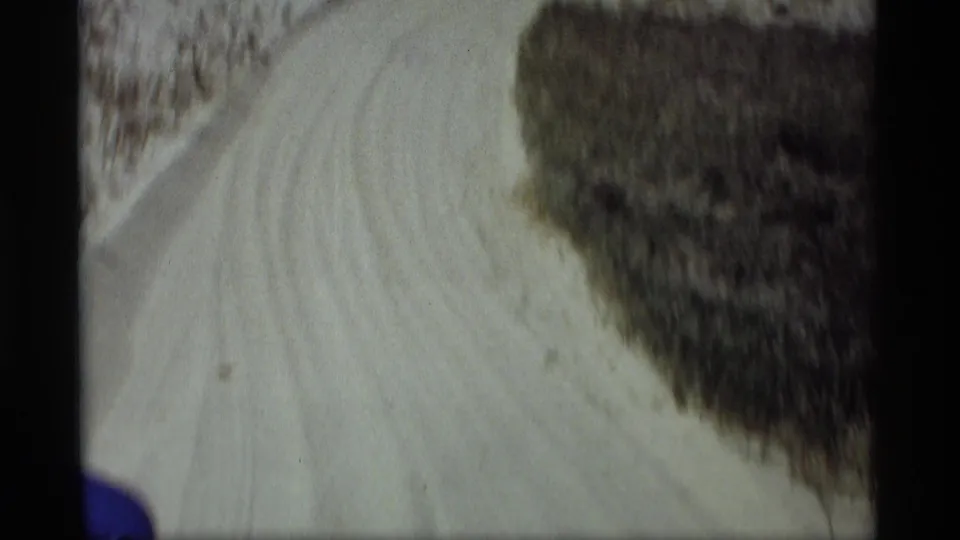 1969 Holland, Michigan 8mm frame showing a pale dirt road bending past roadside brush from a car-travel viewpoint.