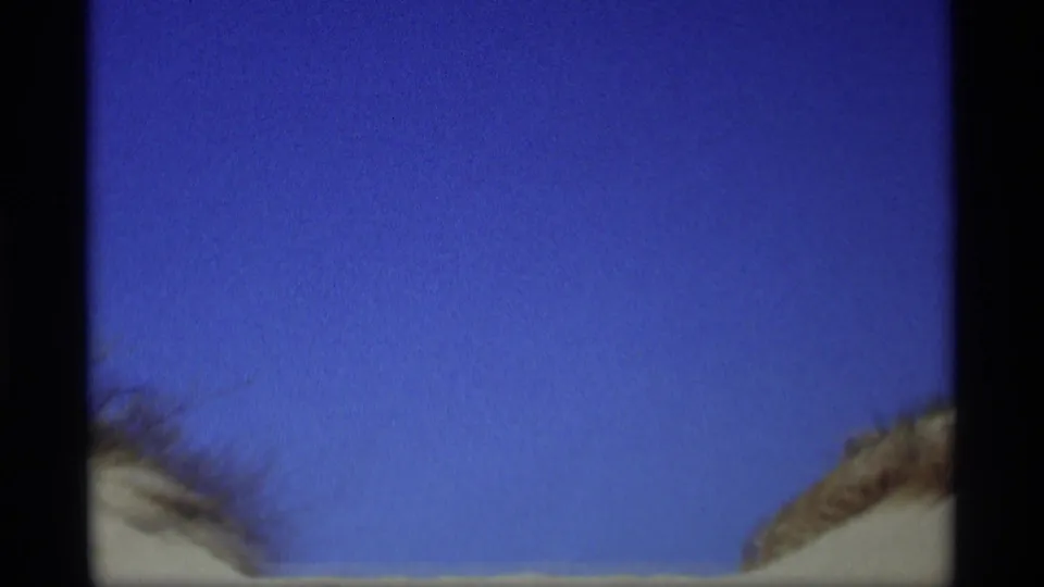 1969 8mm frame from Holland, Michigan showing blue sky above sandy dune edges and heavy gate shadows.