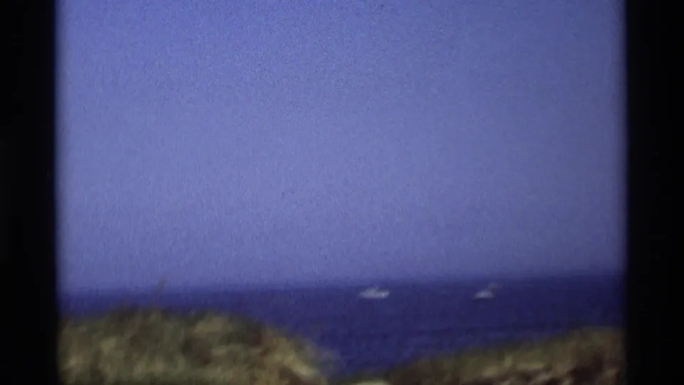 1969 Holland, Michigan 8mm frame showing dune vegetation above blue water with several small distant boats.