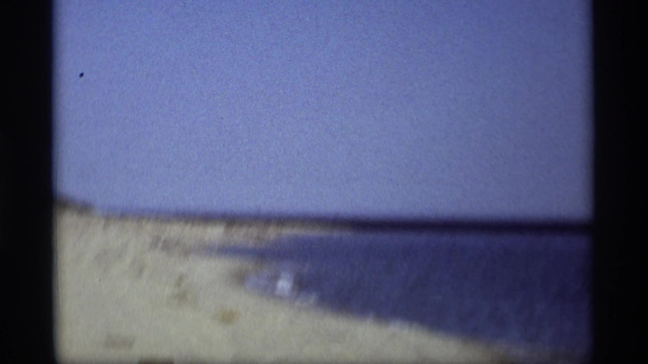 Sandy shoreline meets calm blue water beneath a pale sky.