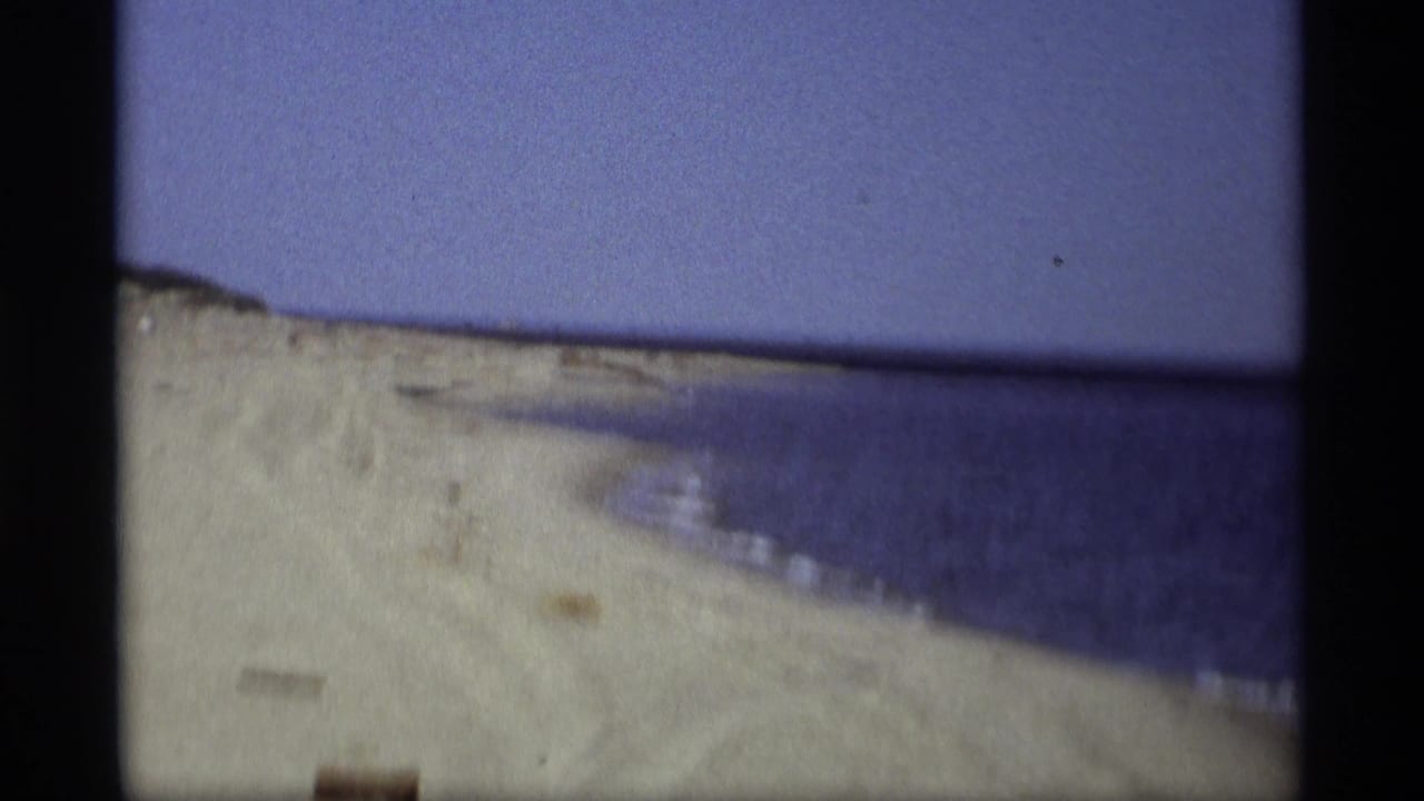 Curving sandy beach beside open water with a clear sky above.